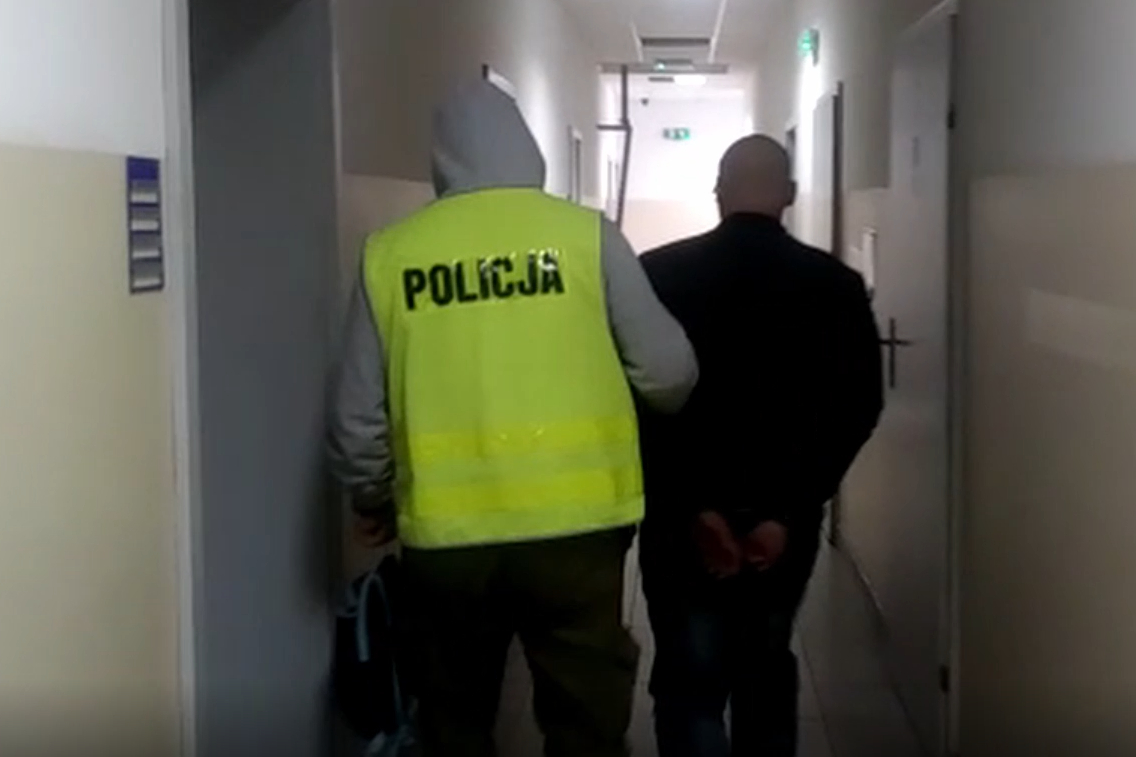 Zatrzymany mężczyzna prowadzony przez policjanta korytarzem w komendzie