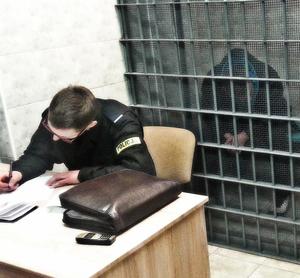 Policjant przy biurku i zatrzymany za kratami