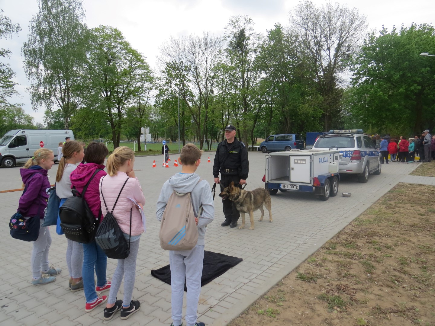 Dzieci wysłuchują policjanta, który prezentuje im psa służbowego