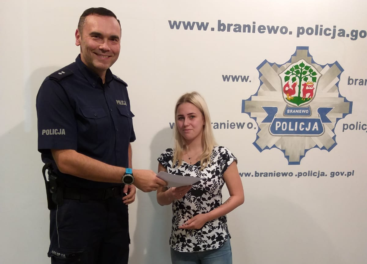 Policjant z Komendy Powiatowej Policji w Braniewie przekazuje odzyskane pieniądze właścicielce