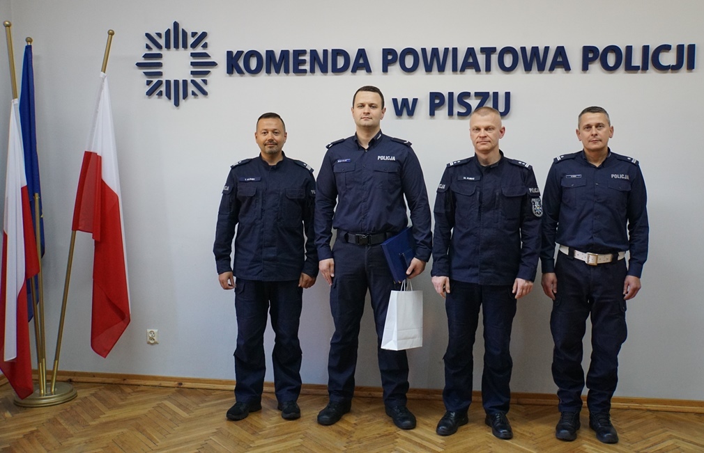 Grupowe zdjęcie Komendanta Wojewódzkiego Policji (od lewej), wyróżnionego policjanta, Komendanta Powiatowego Policji w Piszu oraz Naczelnika Wydziału Prewencji i Ruchu Drogowego KPP w Piszu
