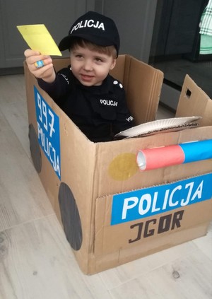 Przebrane za policjanta dziecko w kartonie stylizowanym na dariowóz