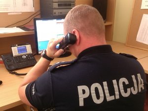 Policjant siedzący przy biurku i trzyma w ręku słuchawkę telefonu