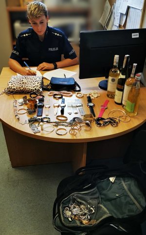 na biurku skradziona biżuteria, torebki, zegarki, alkohol, policjantka spisuje protokół