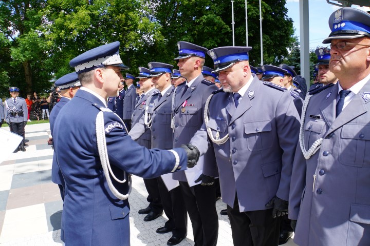 Awansowany policjant stojący w szeregu odbiera akt mianowania i gratulacje od komendanta