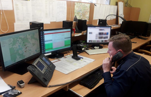 Oficer dyżurny przy telefonie, siedzący za biurkiem, przed monitorami