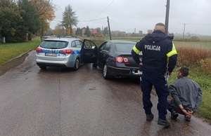 Radiowóz i zatrzymany samochód na drodze, a obok policjant z zatrzymanym mężczyzną