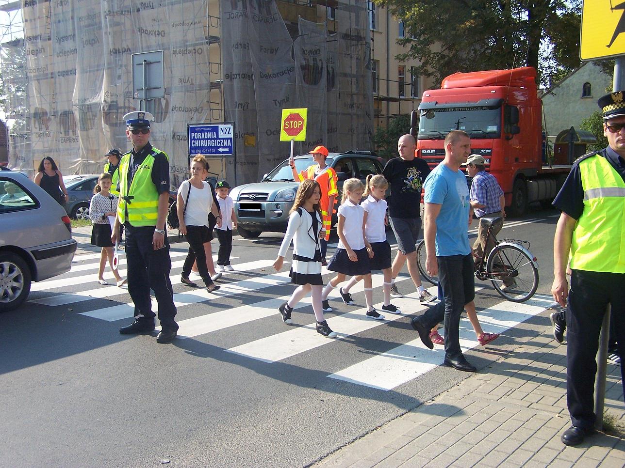 Policjanci pomagają przejść uczniom przez przejście dla pieszych
